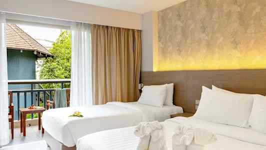 To opdækkede enkeltsenge med dekorative håndklæder og blomster. Udsigt over en møbleret altan med grønne områder og bygning. (AI-genereret tekst)