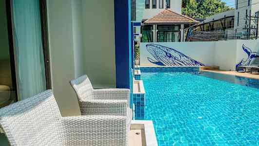 To hvide stole står på en terrasse ved siden af en swimmingpool. På væggen ved poolen er der blå malerier af hvaler. (AI-genereret tekst)