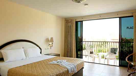 Et hotelværelse med en dobbeltseng, natbord, glasdøre og en balkon med stole. (AI-genereret tekst)