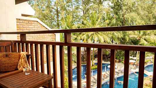 Udsigt fra en altan mod en pool og omkringliggende træer. (AI-genereret tekst)