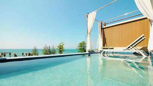 En luksuriøs pool med en solseng ved siden af og havudsigt i baggrunden. (AI-genereret tekst)