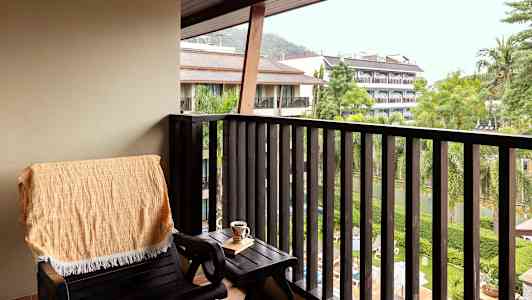 En altan med en stol, et bord og udsigt over grønne områder og bygninger. (AI-genereret tekst)