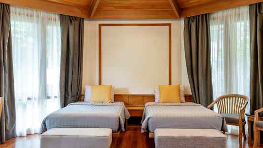 Hotelværelse med to enkeltsenge, træmøbler og store vinduer med gardiner. (AI-genereret tekst)