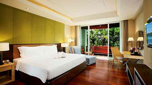 Soveværelse med en stor seng, siddegruppe og skrivebord samt adgang til en balkon med udsigt over en have. (AI-genereret tekst)