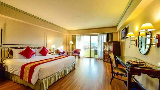 Et hotelværelse med en dobbeltseng og rød dekoration, siddeområde ved altandøren og skrivebord med spejl. (AI-genereret tekst)