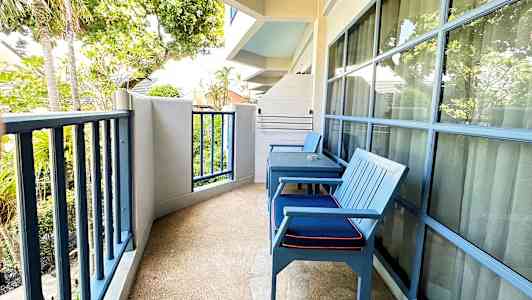 Billede af en altan med to blå stole, bord og udsigt mod træer og grønne områder. (AI-genereret tekst)