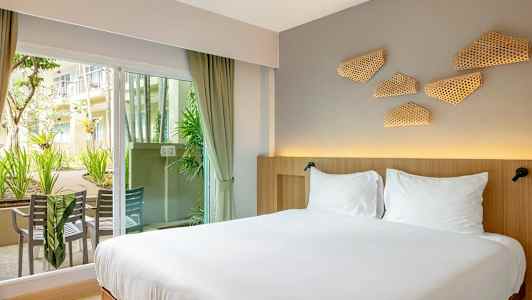 Foto af et hotelværelse med en dobbeltseng nær en glasdør, der fører ud til en udendørsterrasse med siddepladser. (AI-genereret tekst)