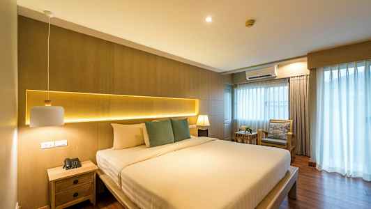 Soveværelse med en stor seng, sidebord og vindue med gardiner. (AI-genereret tekst)