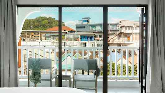 Udsigt gennem en stor glasrude, der åbner ud mod en balkon med udsigt over bymiljøet. (AI-genereret tekst)