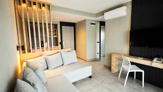 Et moderne hotelværelse med sofa, tv og skrivebord samt en skillevæg for køkkenområdet. (AI-genereret tekst)