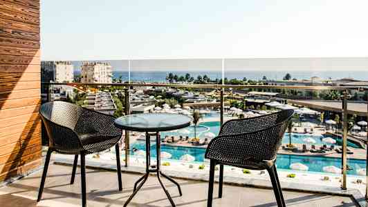 Altan med to stole og et glasbord, udsigt over poolområde og hav. (AI-genereret tekst)