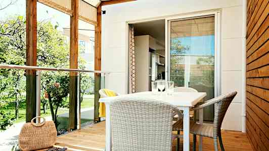 En veranda med tag, bord og stole samt udsigt til en have. (AI-genereret tekst)