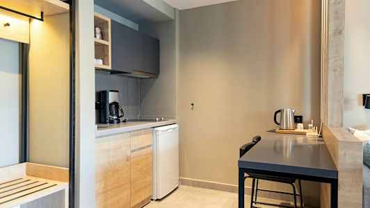 Et køkken med træsbeklædning, kaffemaskine, køleskab og et bord med en vandkedel. (AI-genereret tekst)