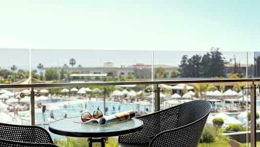 Udsigt fra en balkon mod et poolområde med parasoller, omgivet af grønne omgivelser. (AI-genereret tekst)