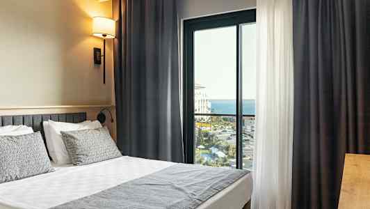 Et hotelværelse med en dobbeltseng og en balkon med udsigt over havet. (AI-genereret tekst)