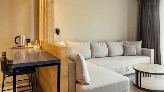 Rum med siddeområde, grå sofa og et bord samt en bardisk med stole. (AI-genereret tekst)