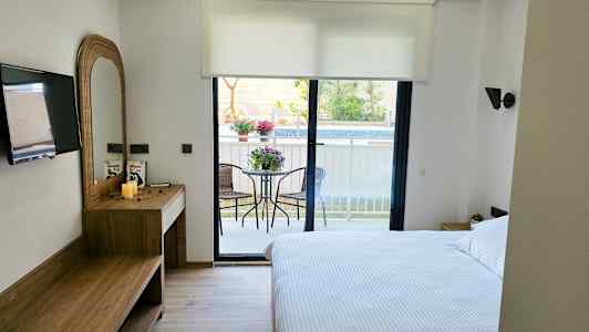 Et hotelværelse med en dobbeltseng, skrivebord, TV og en altan med havemøbler. (AI-genereret tekst)