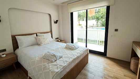 Et soveværelse med en dobbeltseng, et vindue, der vender ud mod en terrasse og en pool. (AI-genereret tekst)