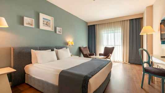 Et hotelværelse med en dobbeltseng, to lænestole ved et bord, et skrivebord og et fjernsyn. (AI-genereret tekst)