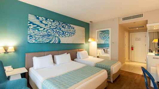 To senge med hvidt sengetøj i et hotelværelse med turkise detaljer og moderne indretning. (AI-genereret tekst)