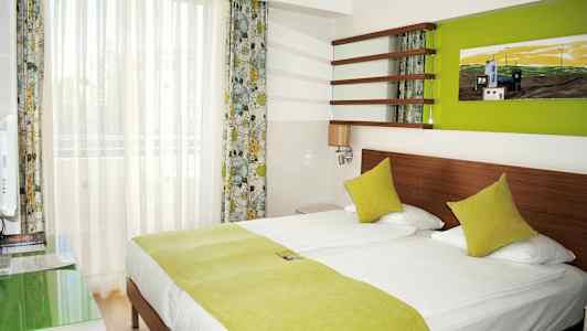 Et hotelværelse med en dobbeltseng og grønne sengelagner. (AI-genereret tekst)