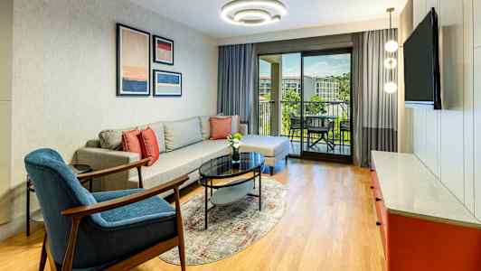 En stue med sofa, lænestol, sofabord og udsigt til en balkon. (AI-genereret tekst)