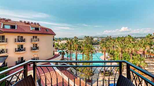 Udsigt fra en altan over en hotelbygning, en pool og palmetræer. (AI-genereret tekst)