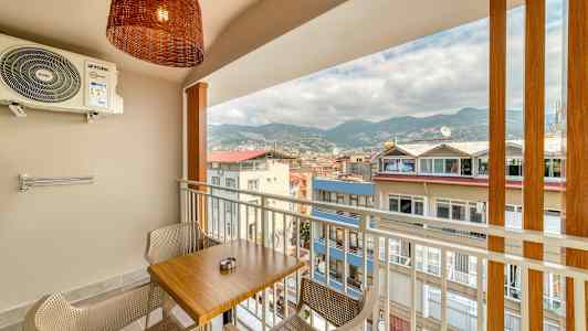 Altan med et bord og to stole, udsigt over bygninger og bjerge. (AI-genereret tekst)