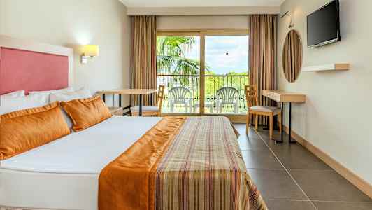 Interiør af et hotelværelse med en stor seng, en altan med havemøbler og et TV på væggen. (AI-genereret tekst)