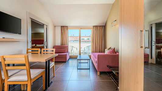 Stue med røde sofaer, et spisebord og stole, et fjernsyn på væggen og altandøre, der fører til en terrasse. (AI-genereret tekst)