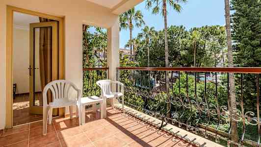 Altan med en dør, to hvide plastikstole og udsigt over træer og vegetation. (AI-genereret tekst)