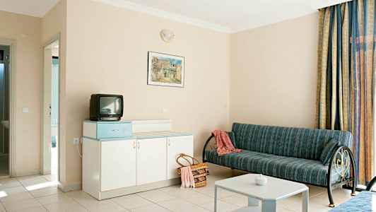 Hotelværelse med sofa, bord, skab og lille tv. (AI-genereret tekst)