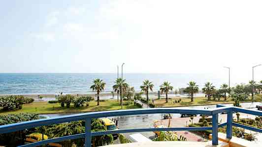 Udsigt fra en altan mod en kystlinje med palmer og hav. (AI-genereret tekst)