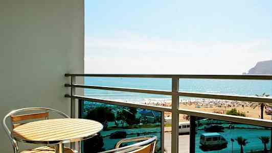 Altan med et bord og to stole, udsigt over stranden og havet. (AI-genereret tekst)