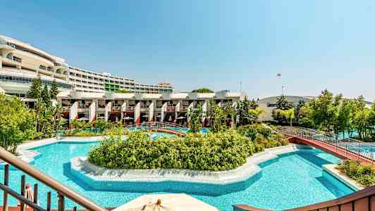 Billede af en hotelpool med frodige planter og udsigt over bygninger i baggrunden. (AI-genereret tekst)