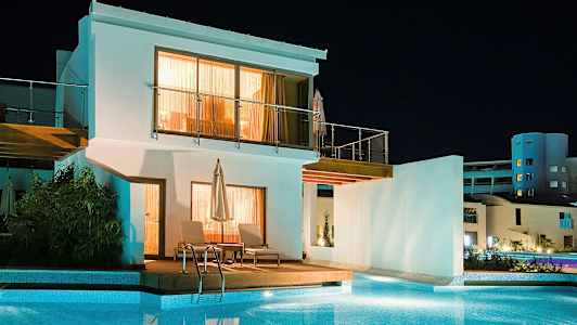 Hvid bygning med pool foran, taget om aftenen. (AI-genereret tekst)