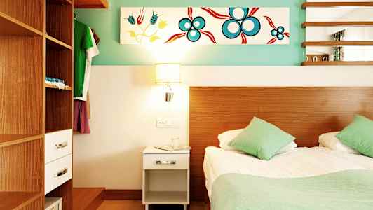 Et soveværelse med en seng, to grønne puder, et træbeklædt skab og et natbord med en lampe. (AI-genereret tekst)