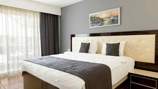 Et moderne hotelværelse med en dobbeltseng, en grå sengeklæde og et maleri på væggen. (AI-genereret tekst)