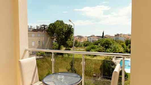 Udsigt fra en altan med bord og stole, mod grønne omgivelser og et boligområde. (AI-genereret tekst)