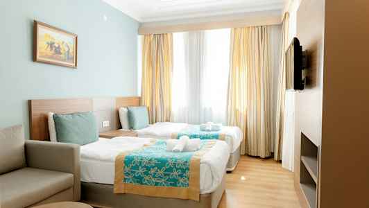 Hotelværelse med to enkeltsenge, en sofa og et tv på væggen. (AI-genereret tekst)