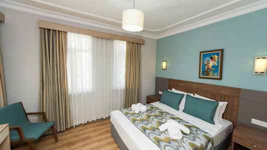 Hotelværelse med dobbeltseng, sengelamper, et maleri på væggen og en stol ved vinduet. (AI-genereret tekst)