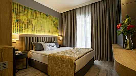 Et hotelværelse med en dobbeltseng, grå gardiner og et maleri over sengen. (AI-genereret tekst)