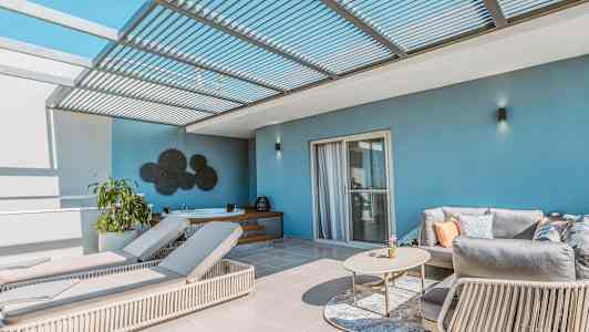 En terrasse med liggestole, sofa og bord under et pergolatag. (AI-genereret tekst)