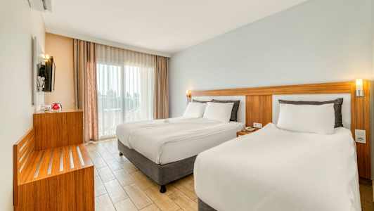 Moderne hotelværelse med to senge, lyse farver og store vinduer. (AI-genereret tekst)