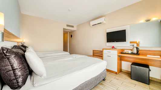 Et hotelværelse med to senge, et skrivebord, et spejl og et vægmonteret TV. (AI-genereret tekst)