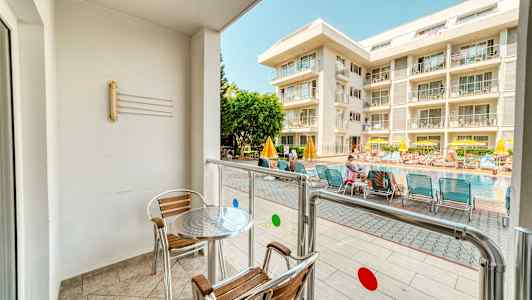 En balkon med bord og stole vender mod en pool og et hotel. (AI-genereret tekst)