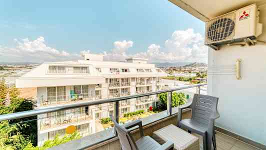 Udsigt fra en altan med stole og bord, med udsyn til en boligbygning. (AI-genereret tekst)