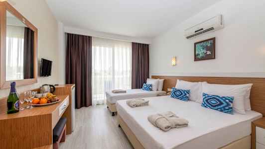Hotelværelse med to enkeltsenge redt med hvide lagner og blå puder samt et bord med frugt og drikkevarer. (AI-genereret tekst)