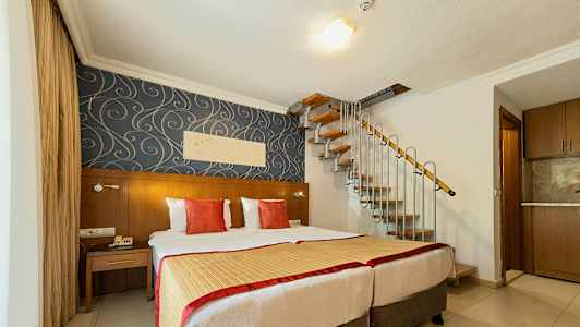 Et hotelværelse med to senge, dekorativt tapet og en vindeltrappe, der fører opad. (AI-genereret tekst)