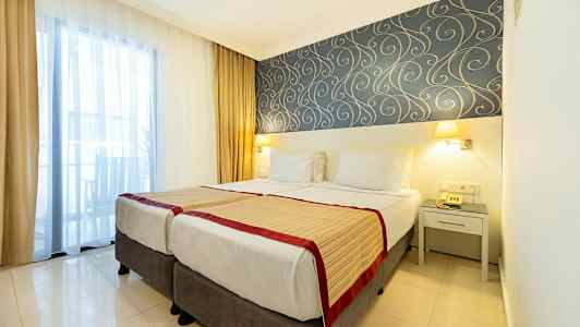 Hotelværelse med to enkeltsenge, dekorativt tapetmønster og vindue med gardiner. (AI-genereret tekst)